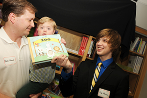 Kye Masino, right, hands a book to Matt Toland and his son Leighton Toland before dedicating the library.